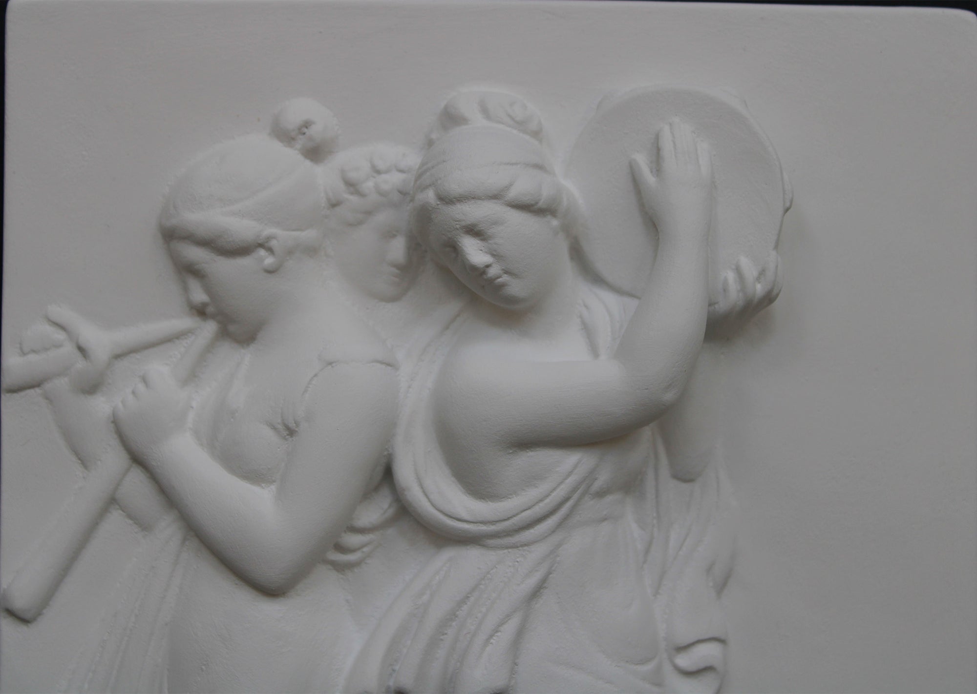 Photo with black background of plaster cast sculpture relief of females playing instruments