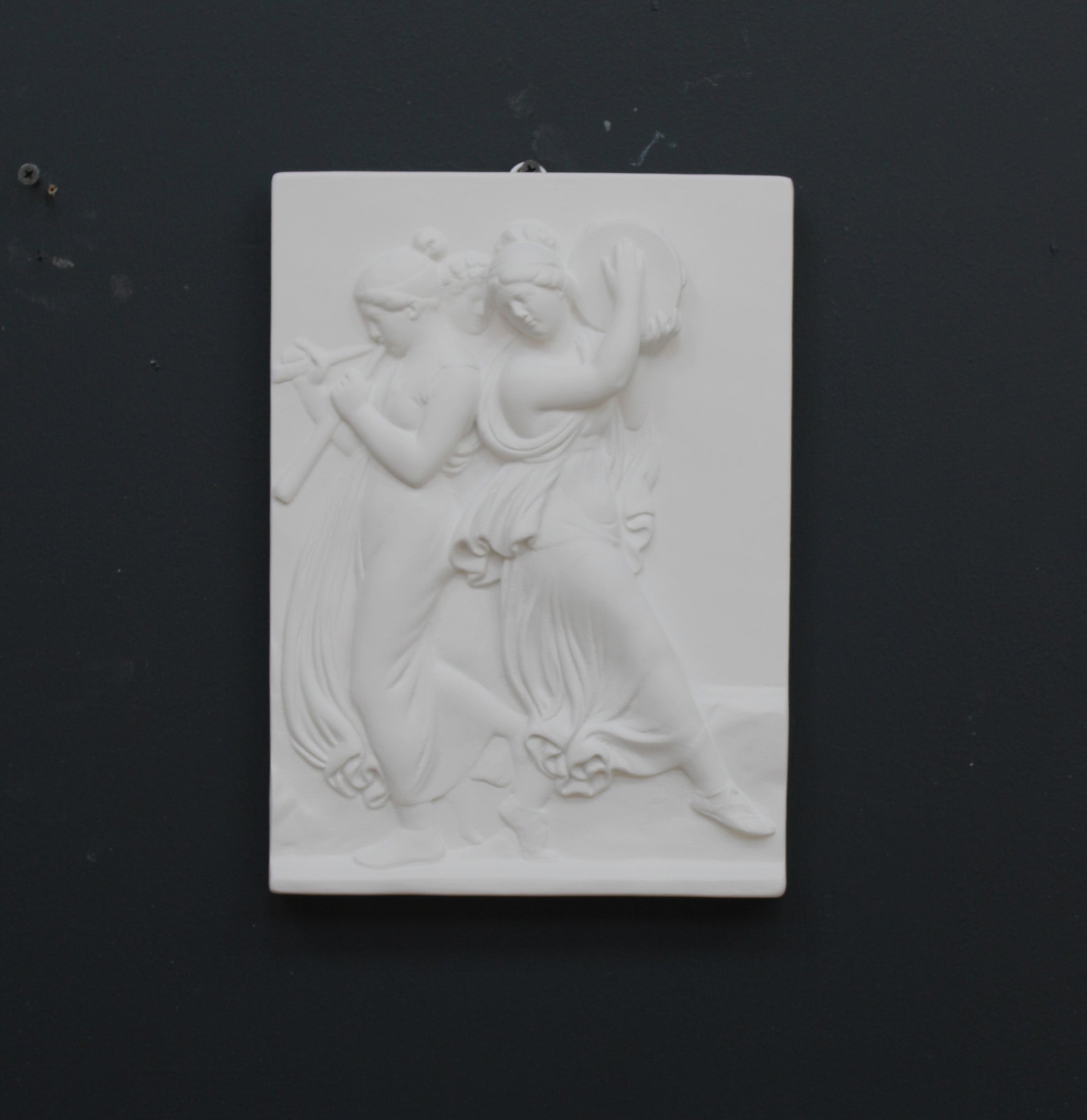 Photo with black background of plaster cast sculpture relief of females playing instruments