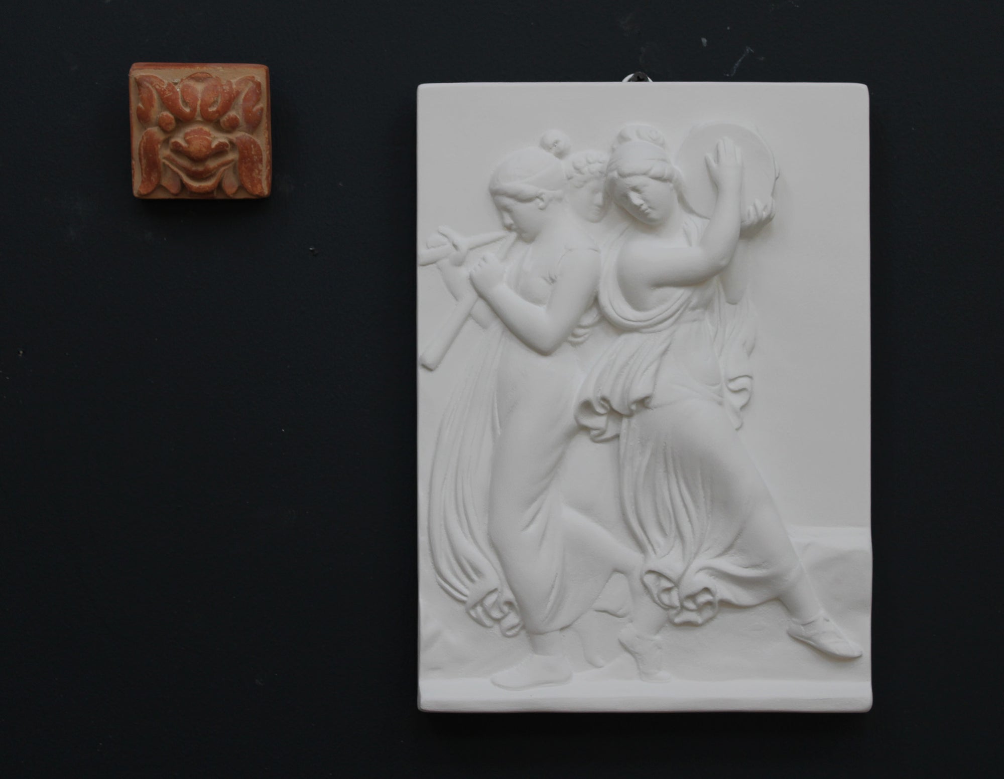 Photo with black background of plaster cast sculpture relief of females playing instruments