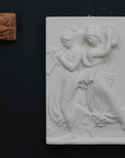 Photo with black background of plaster cast sculpture relief of females playing instruments