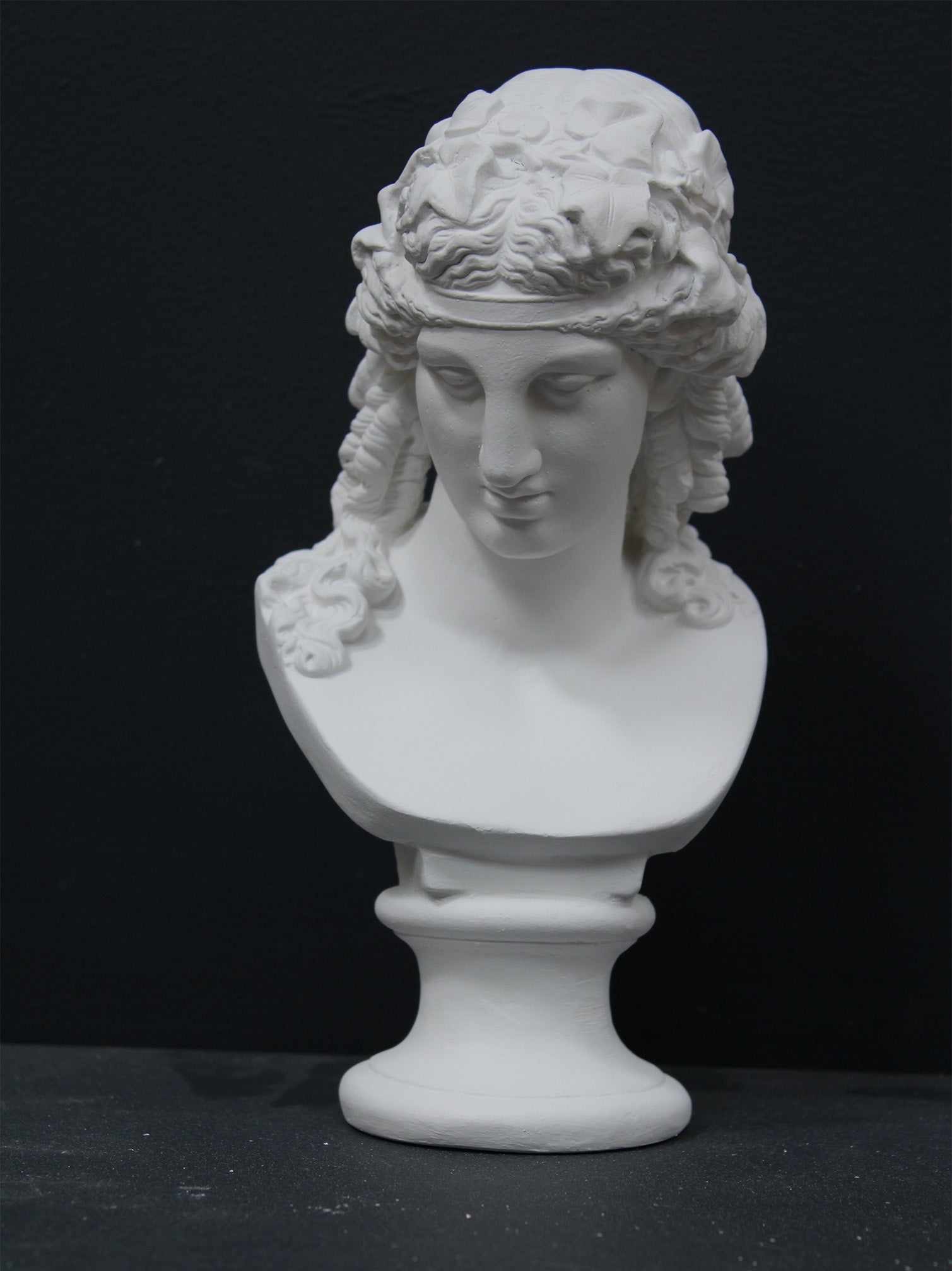 photo of plaster cast of sculpture bust of Ariadne or Bacchus with long, curly hair and head band on a black background