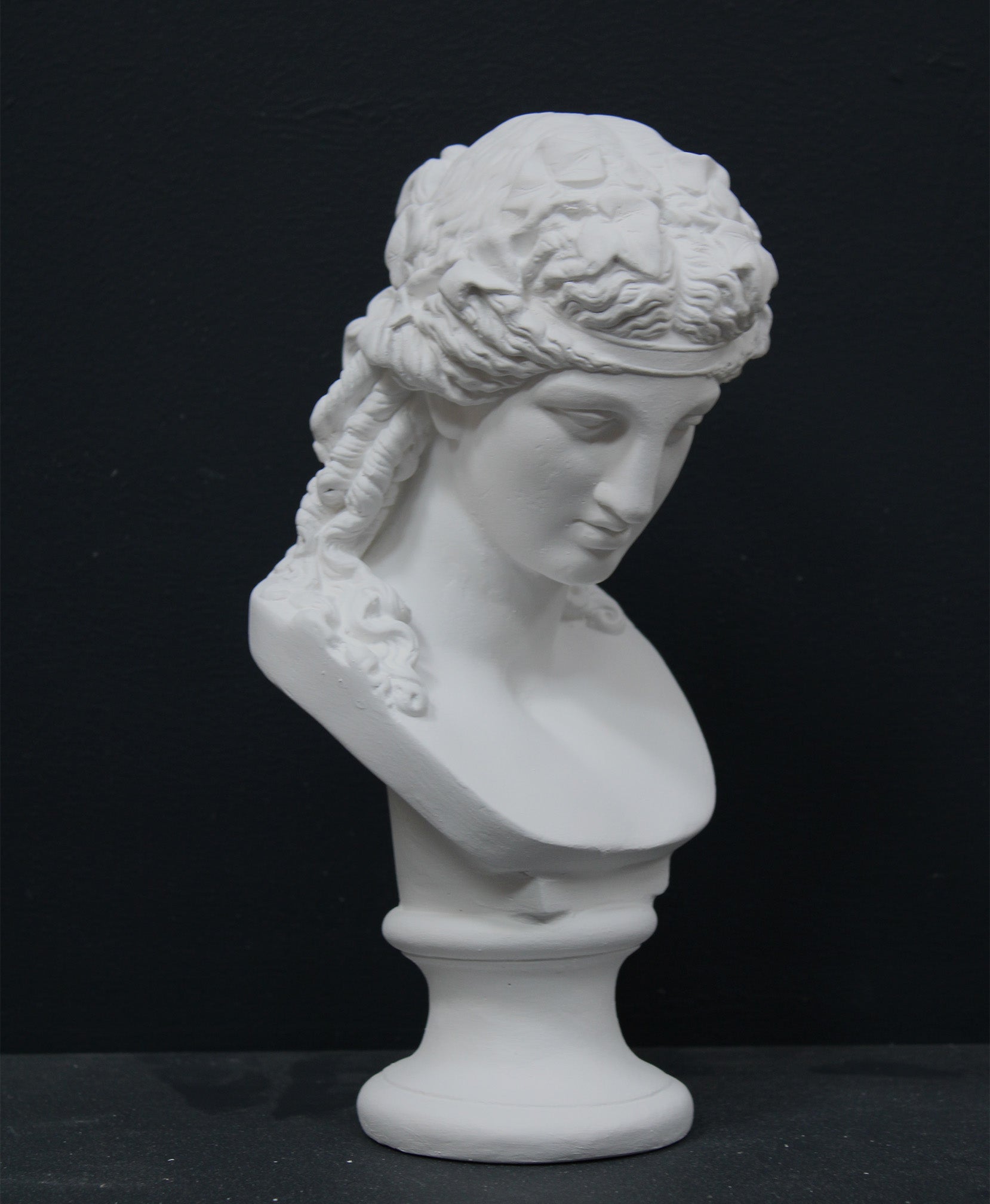 photo of plaster cast of sculpture bust of Ariadne or Bacchus with long, curly hair and head band on a black background