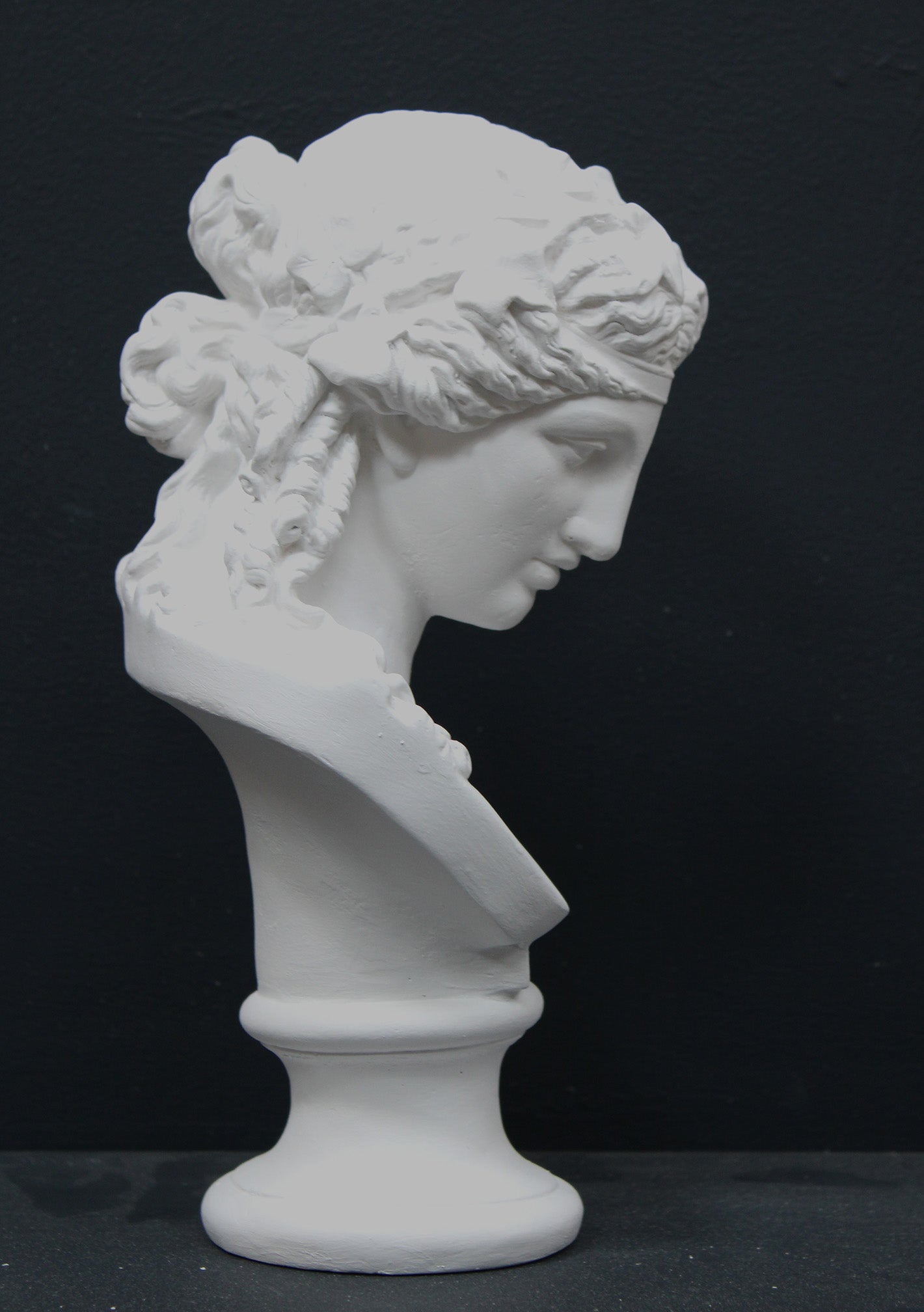 photo of plaster cast of sculpture bust of Ariadne or Bacchus with long, curly hair and head band on a black background