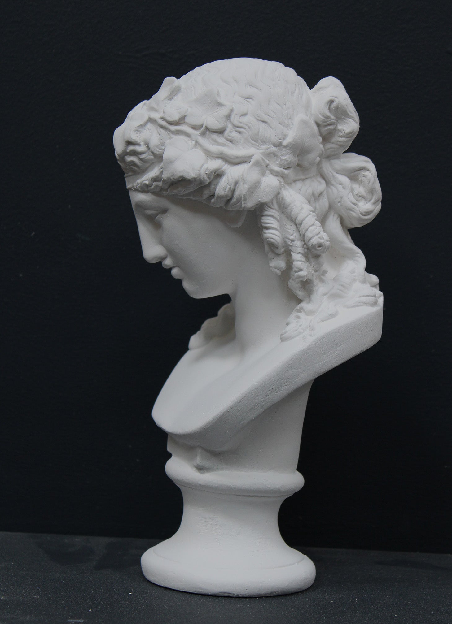 photo of plaster cast of sculpture bust of Ariadne or Bacchus with long, curly hair and head band on a black background