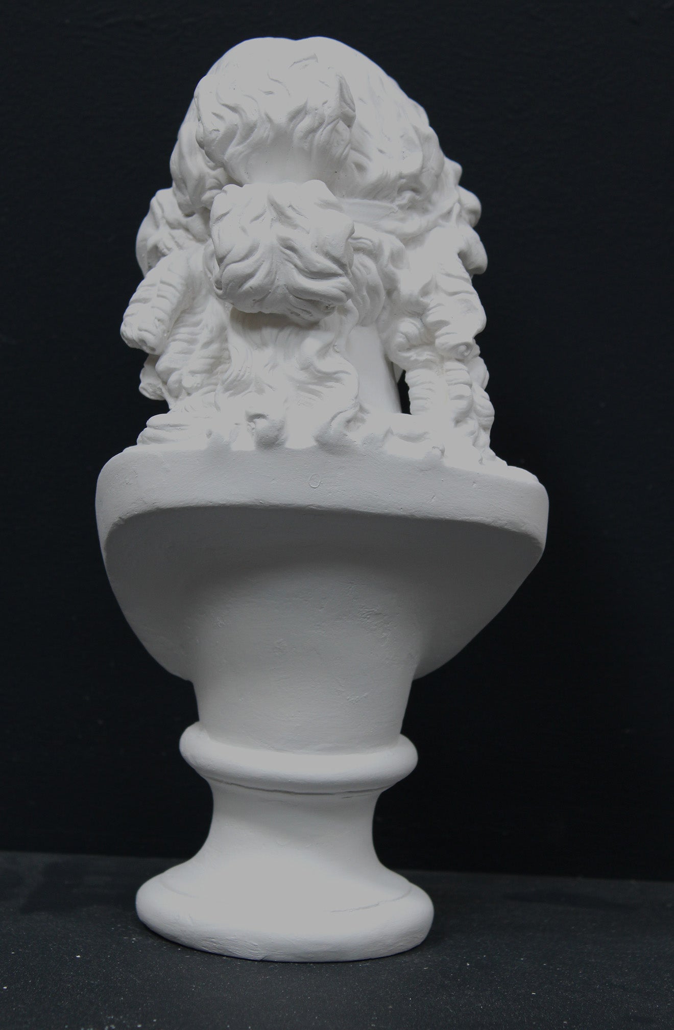 photo of plaster cast of sculpture bust of Ariadne or Bacchus with long, curly hair and head band on a black background