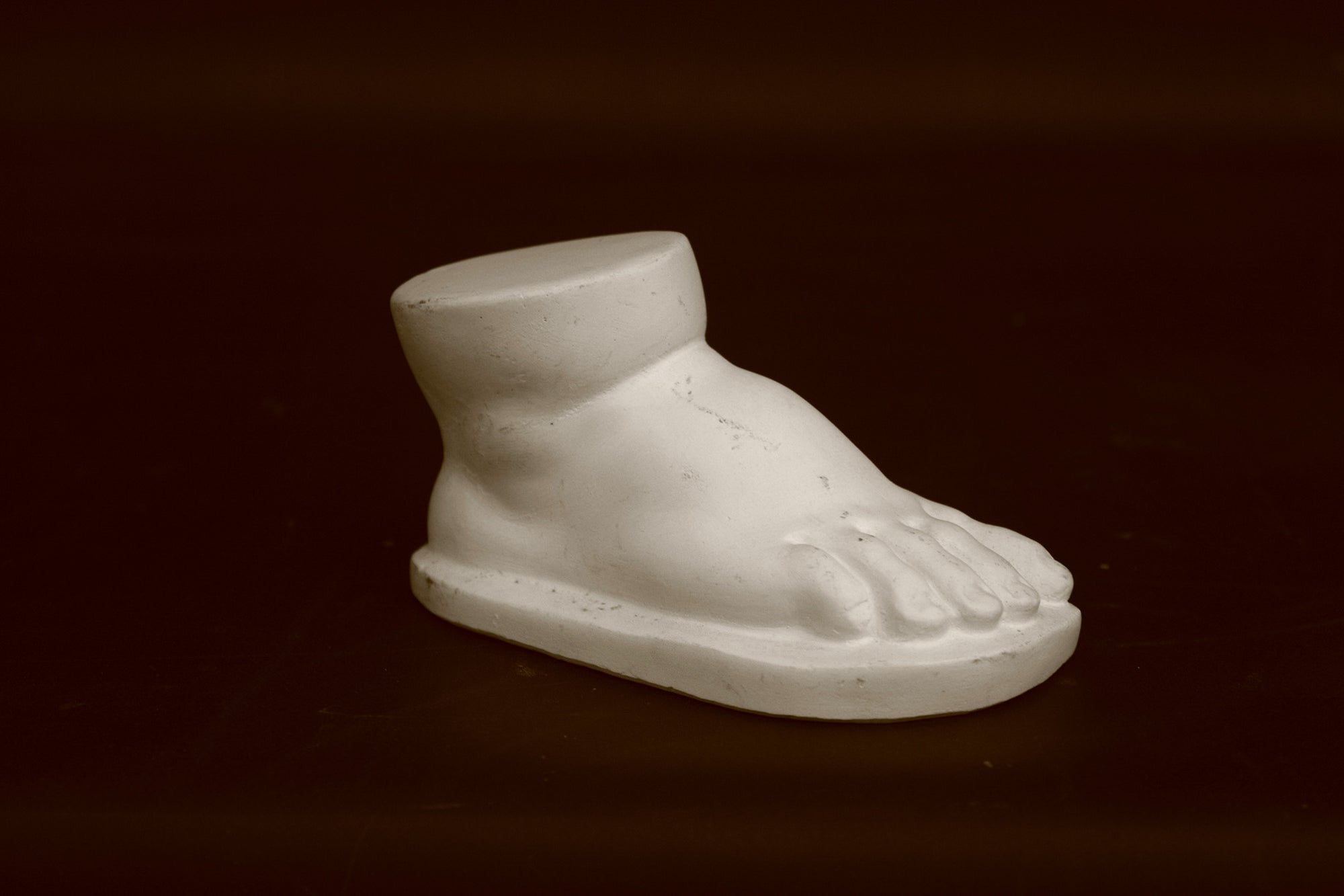 photo of off-white plaster cast sculpture of baby foot against black background
