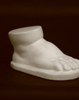 photo of off-white plaster cast sculpture of baby foot against black background