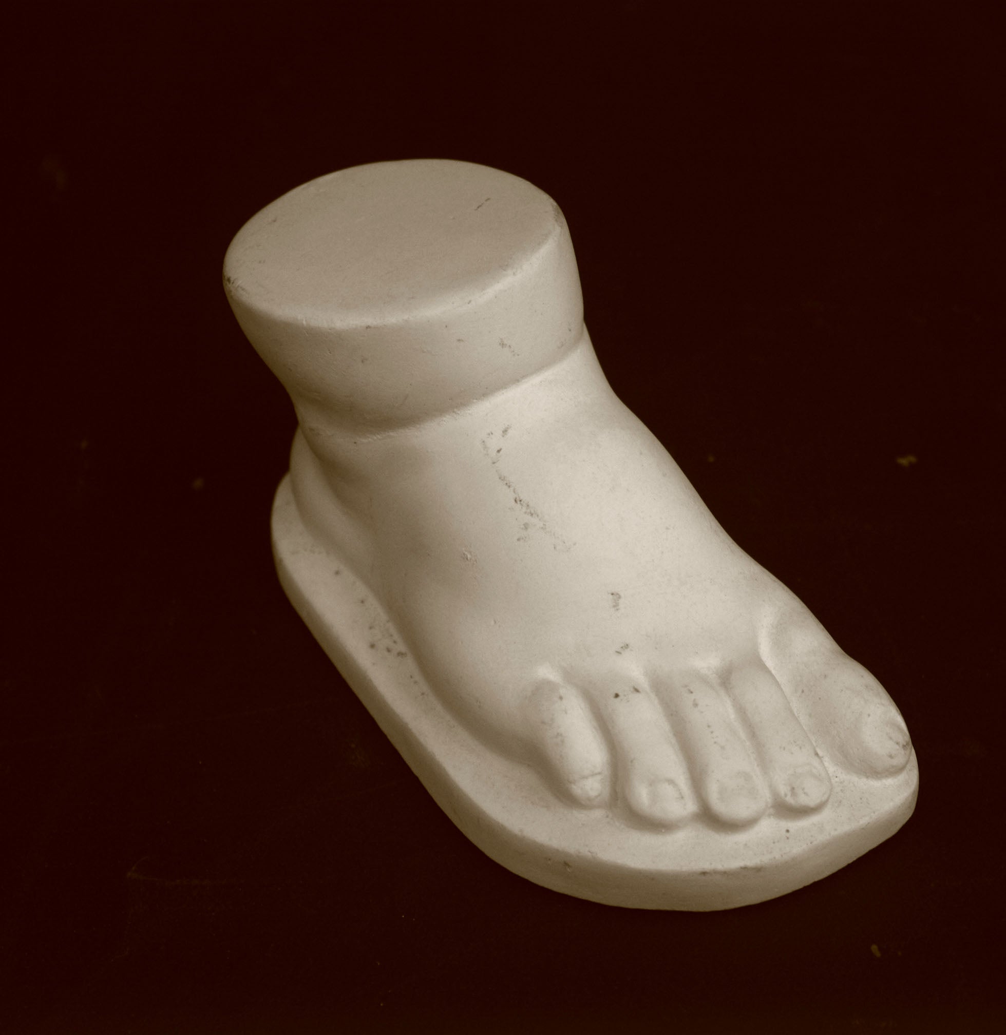 photo of off-white plaster cast sculpture of baby foot against black background