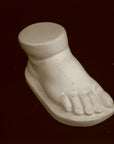 photo of off-white plaster cast sculpture of baby foot against black background