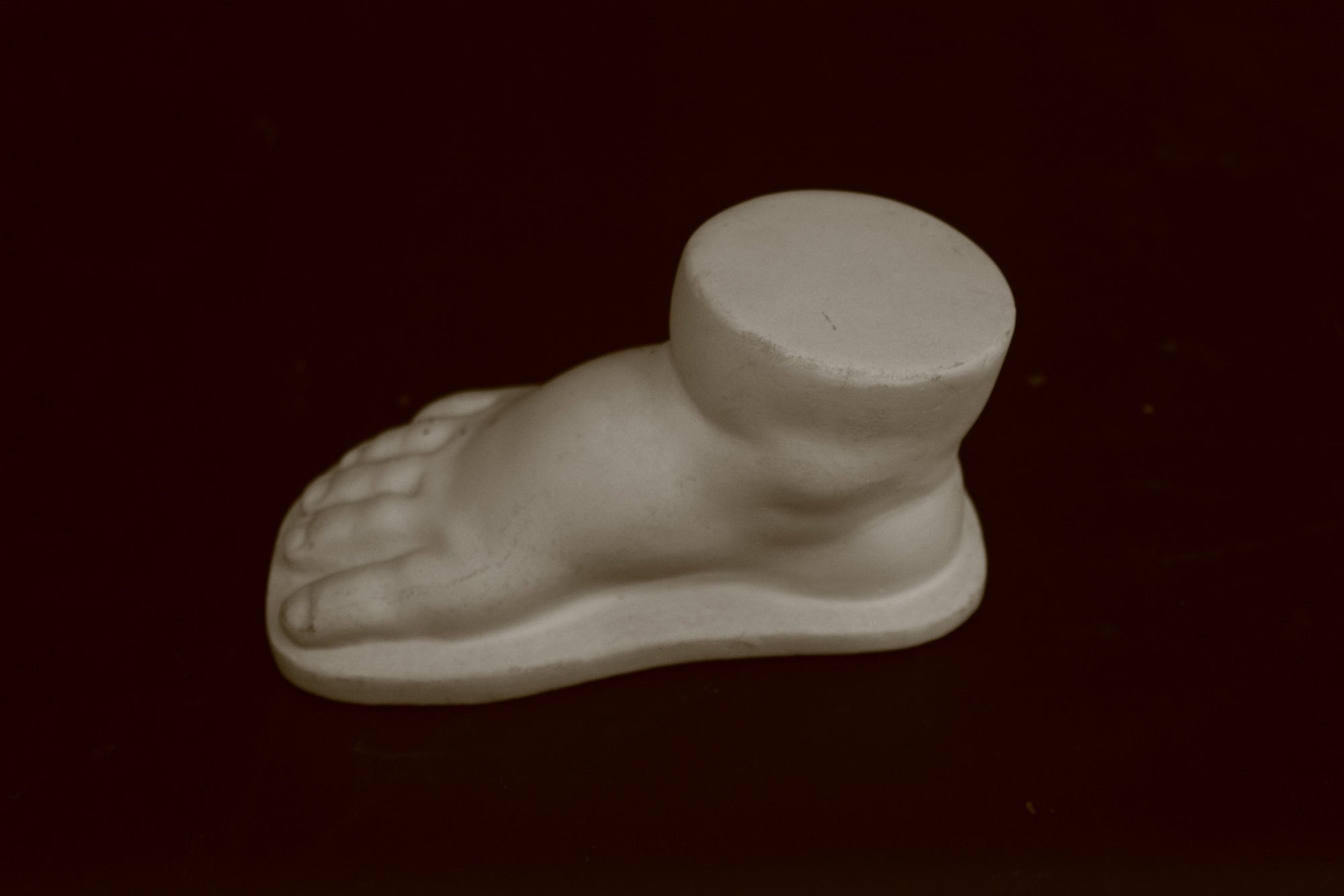 photo of off-white plaster cast sculpture of baby foot against black background