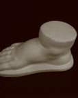 photo of off-white plaster cast sculpture of baby foot against black background