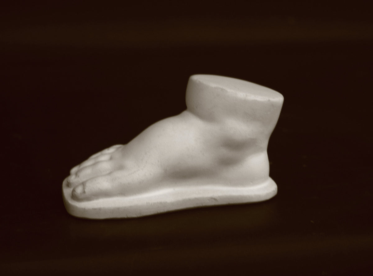 photo of off-white plaster cast sculpture of baby foot against black background