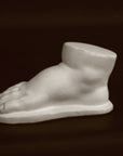 photo of off-white plaster cast sculpture of baby foot against black background
