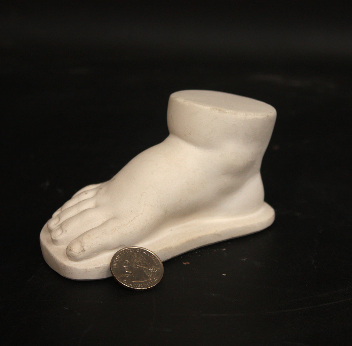 photo of off-white plaster cast sculpture of baby foot against black background