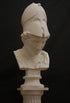 photo of plaster cast sculpture bust of female head, namely the goddess Minerva, with a helmet and looking down and placed on a pedestal with black background