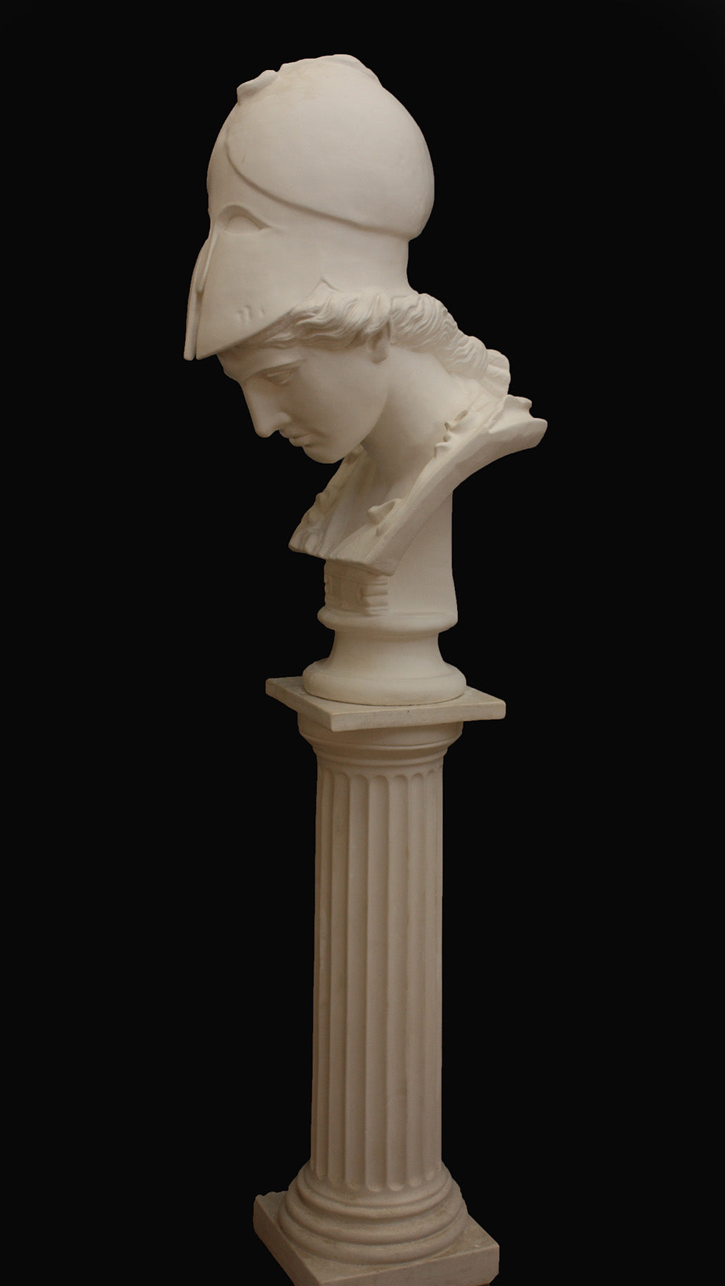photo of plaster cast sculpture bust of female head, namely the goddess Minerva, with a helmet and looking down and placed on a pedestal with black background