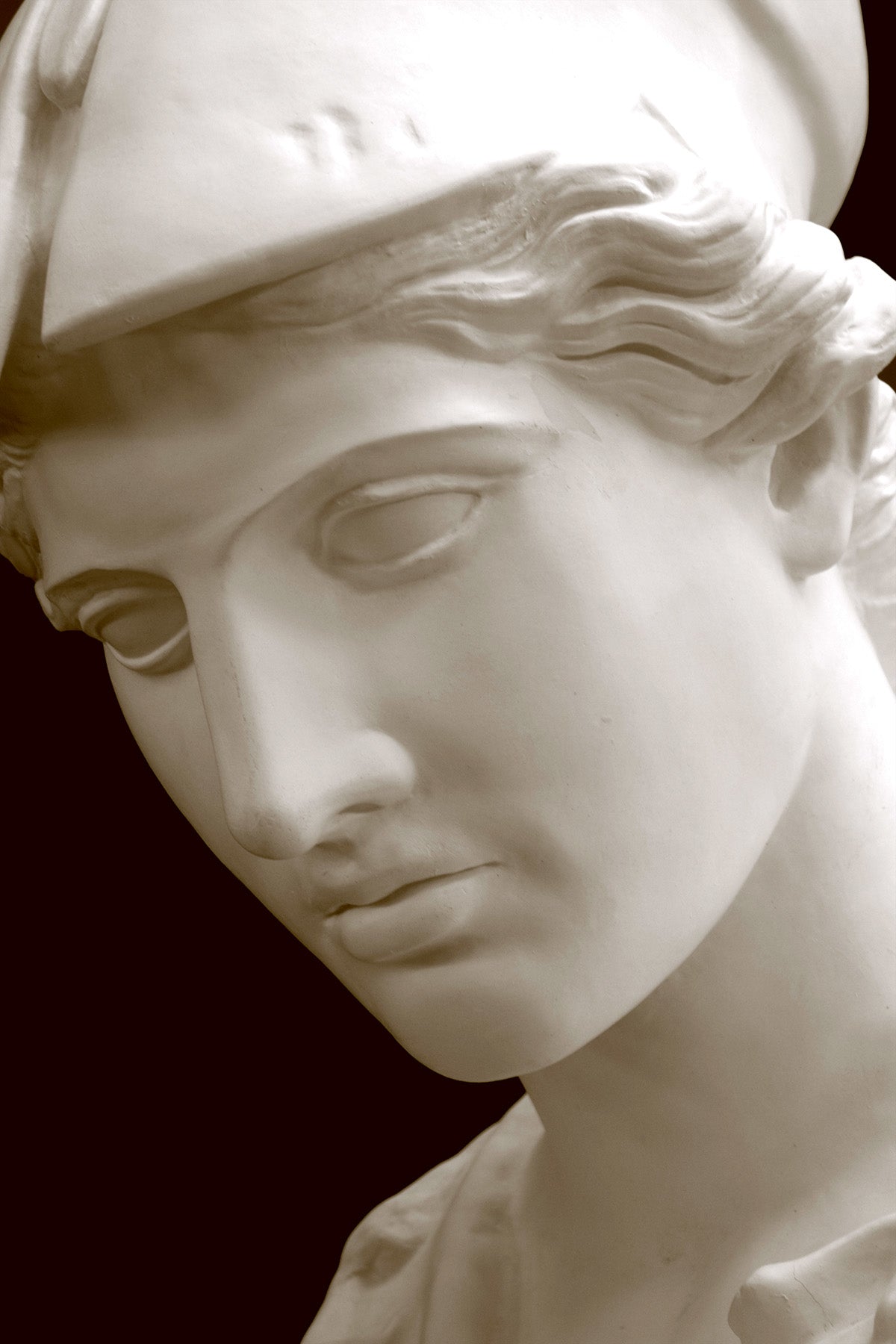 photo of plaster cast sculpture bust of female head, namely the goddess Minerva, with a helmet and looking down with black background