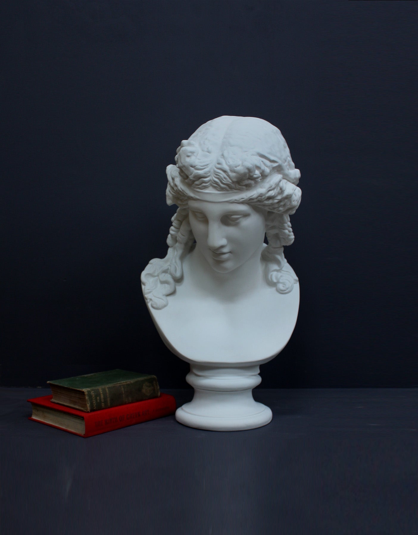 image of a plaster statue of a bust of ariadne next to books on a gray background