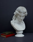 photo of plaster cast of sculpture bust of Ariadne or Bacchus with long, curly hair and head band next to books on a gray background