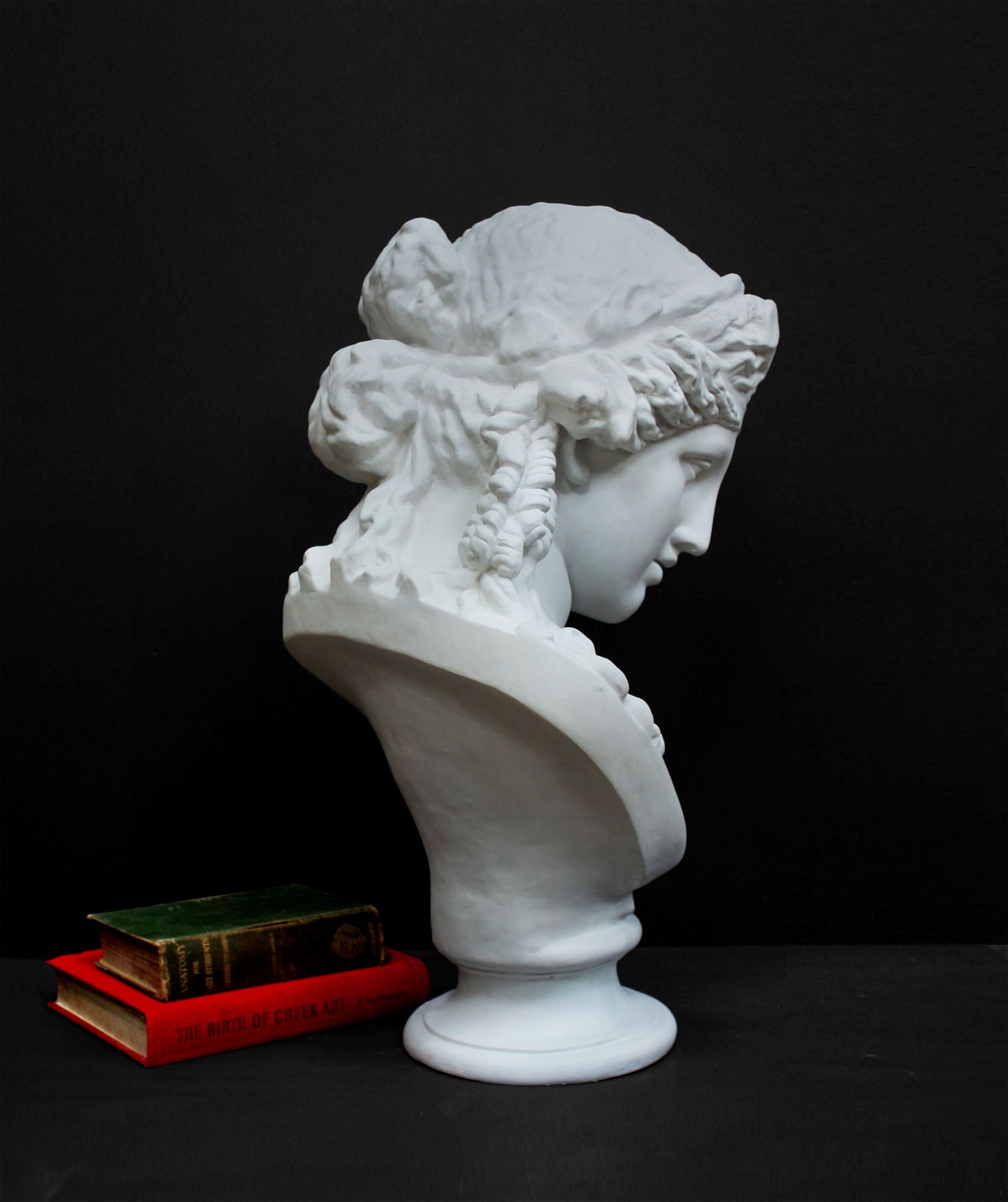 image of a plaster statue of a bust of ariadne next to books on a gray background