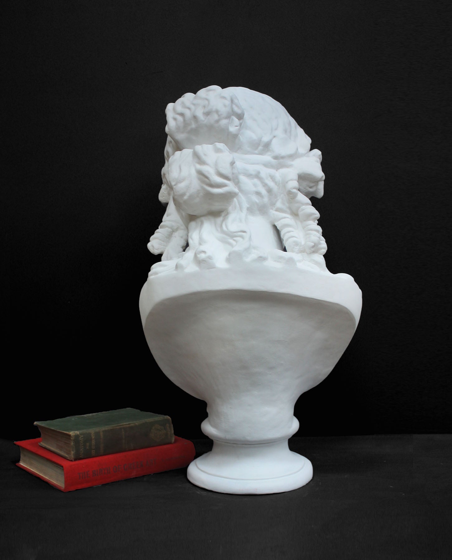 image of a plaster statue of a bust of ariadne next to books on a gray background