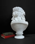 back view photo of plaster cast of sculpture bust of Ariadne or Bacchus with long, curly hair and head band next to books on a gray background
