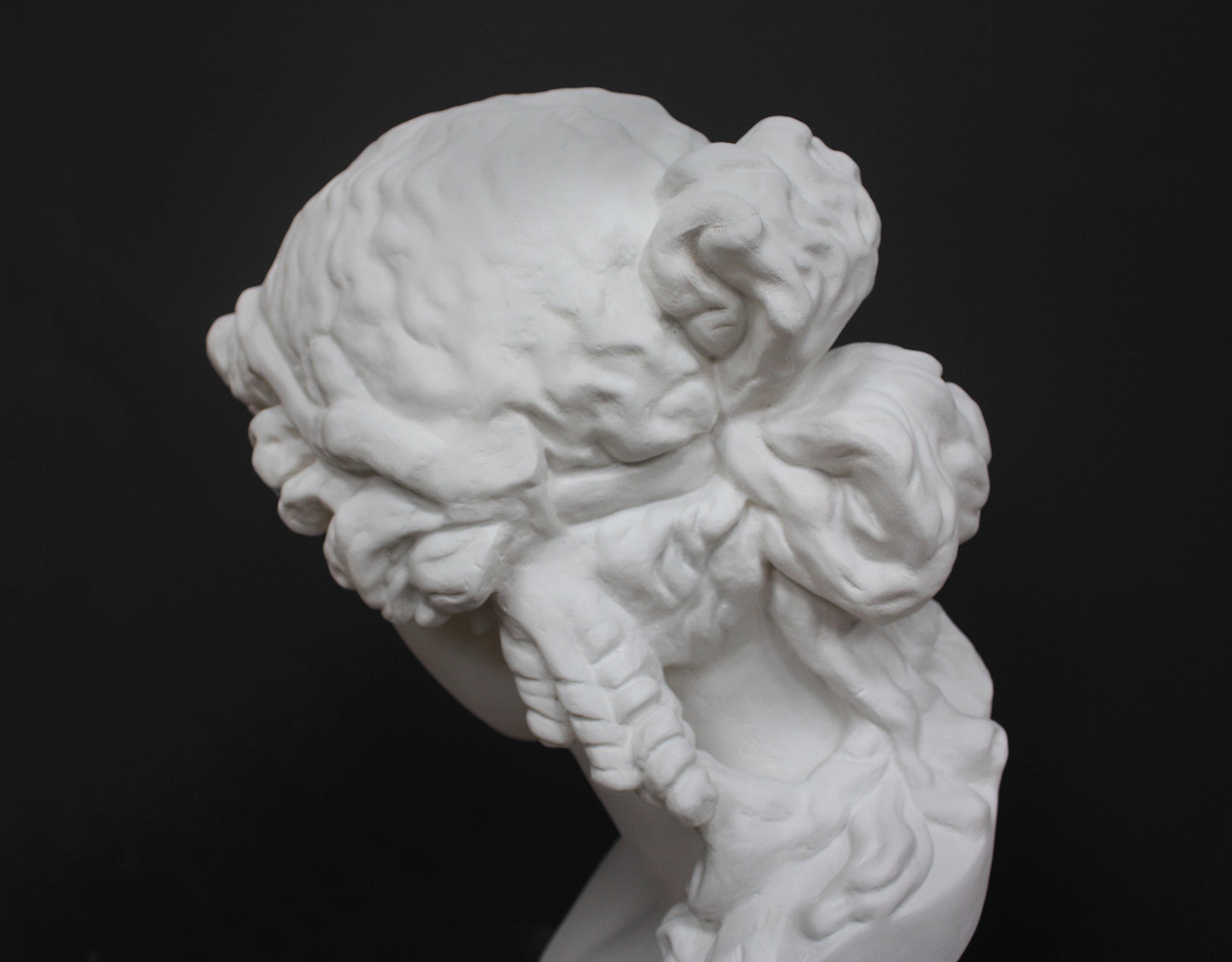 detail photo of plaster cast of sculpture bust of Ariadne or Bacchus with long, curly hair and head band on a gray background