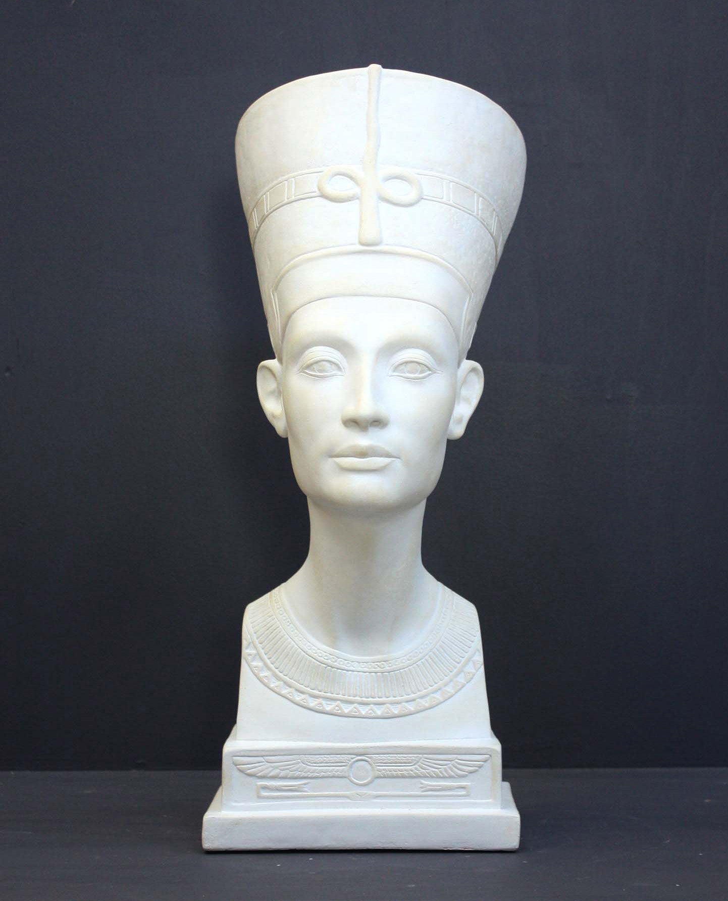 photo of plaster cast sculpture of bust of Nefertiti with crown and decorative collar on a decorative base with a black background