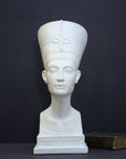 photo of plaster cast sculpture of bust of Nefertiti with crown and decorative collar on a decorative base with a black background