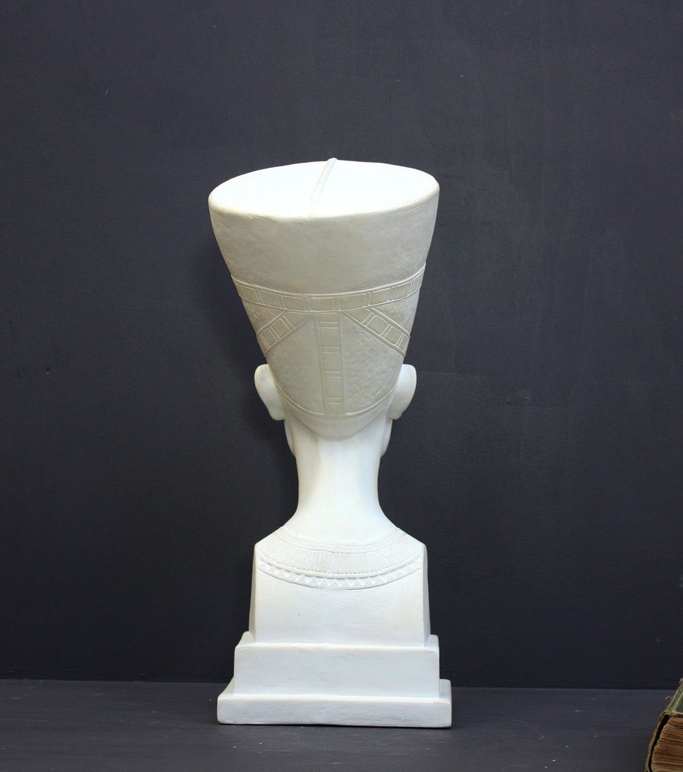 photo of plaster cast sculpture of bust of Nefertiti with crown and decorative collar on a decorative base with a black background