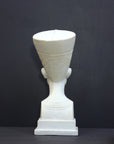 photo of plaster cast sculpture of bust of Nefertiti with crown and decorative collar on a decorative base with a black background