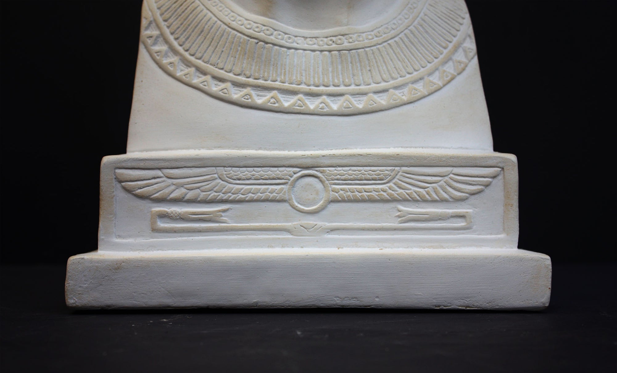 photo of plaster cast sculpture of bust of Nefertiti with crown and decorative collar on a decorative base with a black background