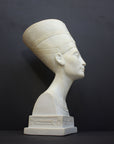 photo of plaster cast sculpture of bust of Nefertiti with crown and decorative collar on a decorative base with a black background