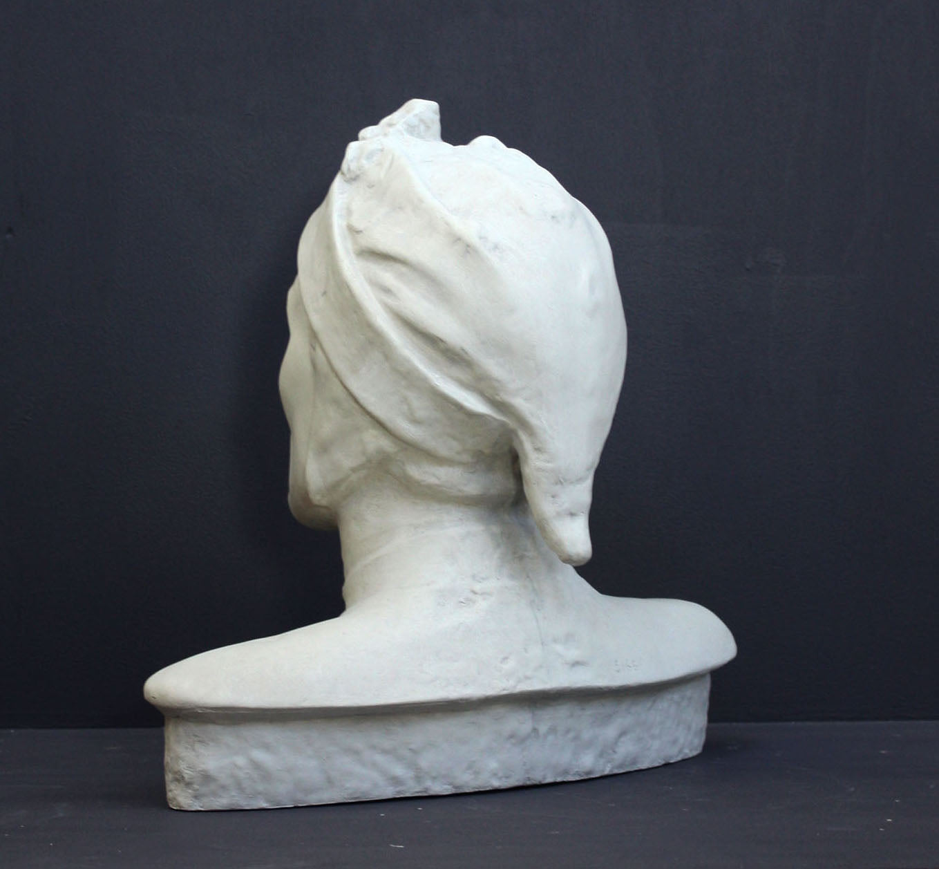 photo of plaster cast bust sculpture of Dante Alighieri with cap and high-necked robe with red book leaning against right side on black background