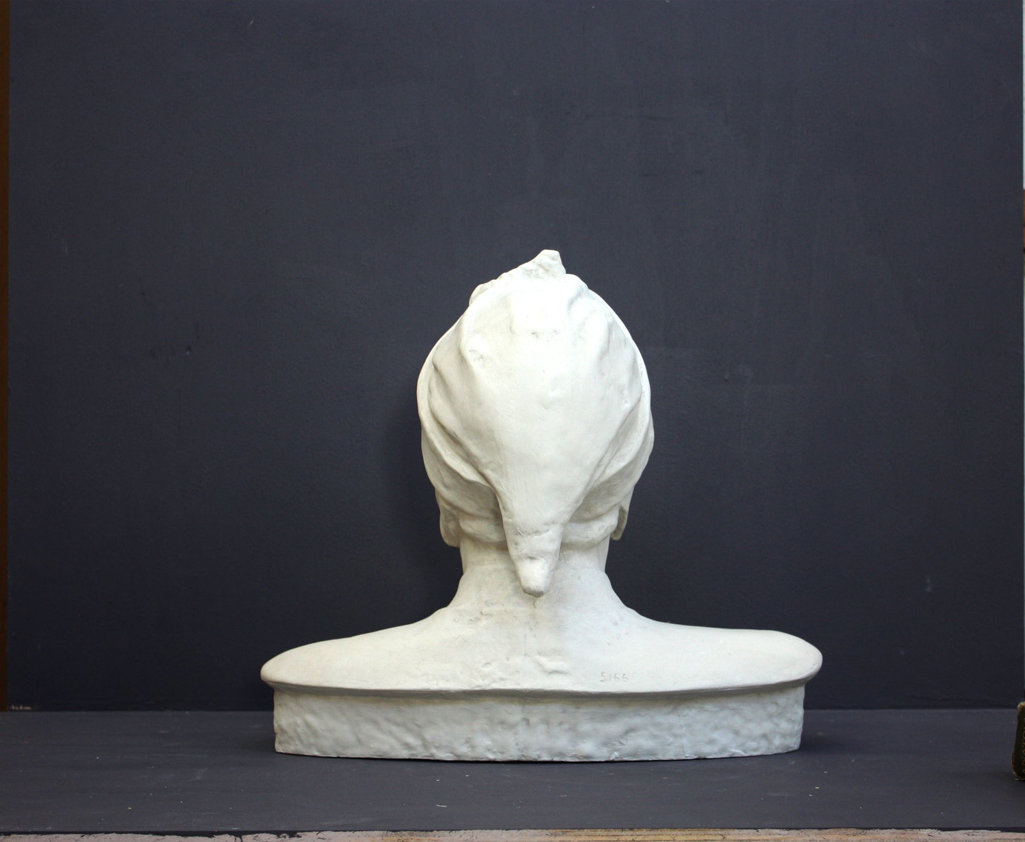 photo of plaster cast bust sculpture of Dante Alighieri with cap and high-necked robe with red book leaning against right side on black background