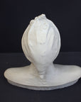 photo of plaster cast bust sculpture of Dante Alighieri with cap and high-necked robe with red book leaning against right side on black background 