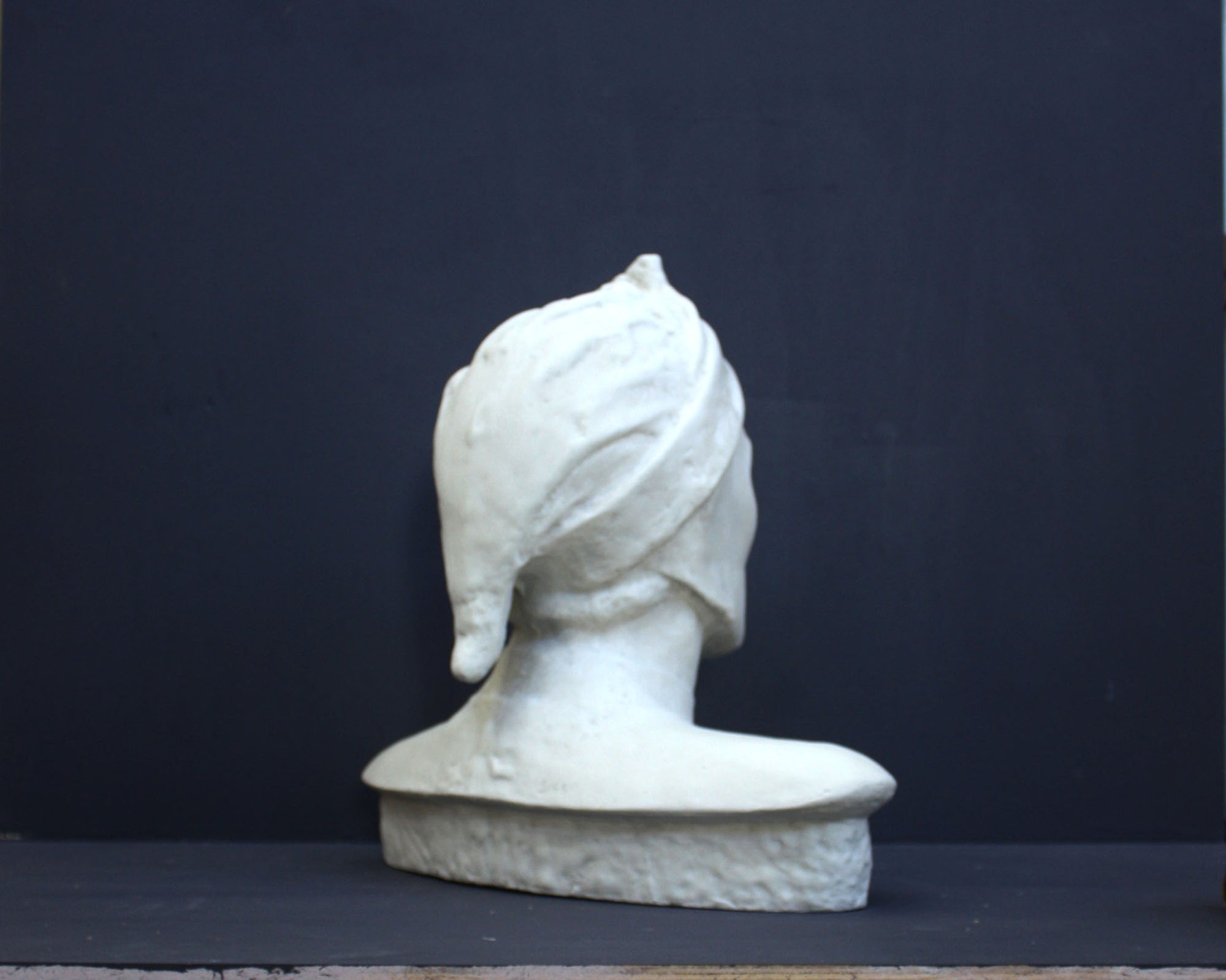 photo of plaster cast bust sculpture of Dante Alighieri with cap and high-necked robe with red book leaning against right side on black background