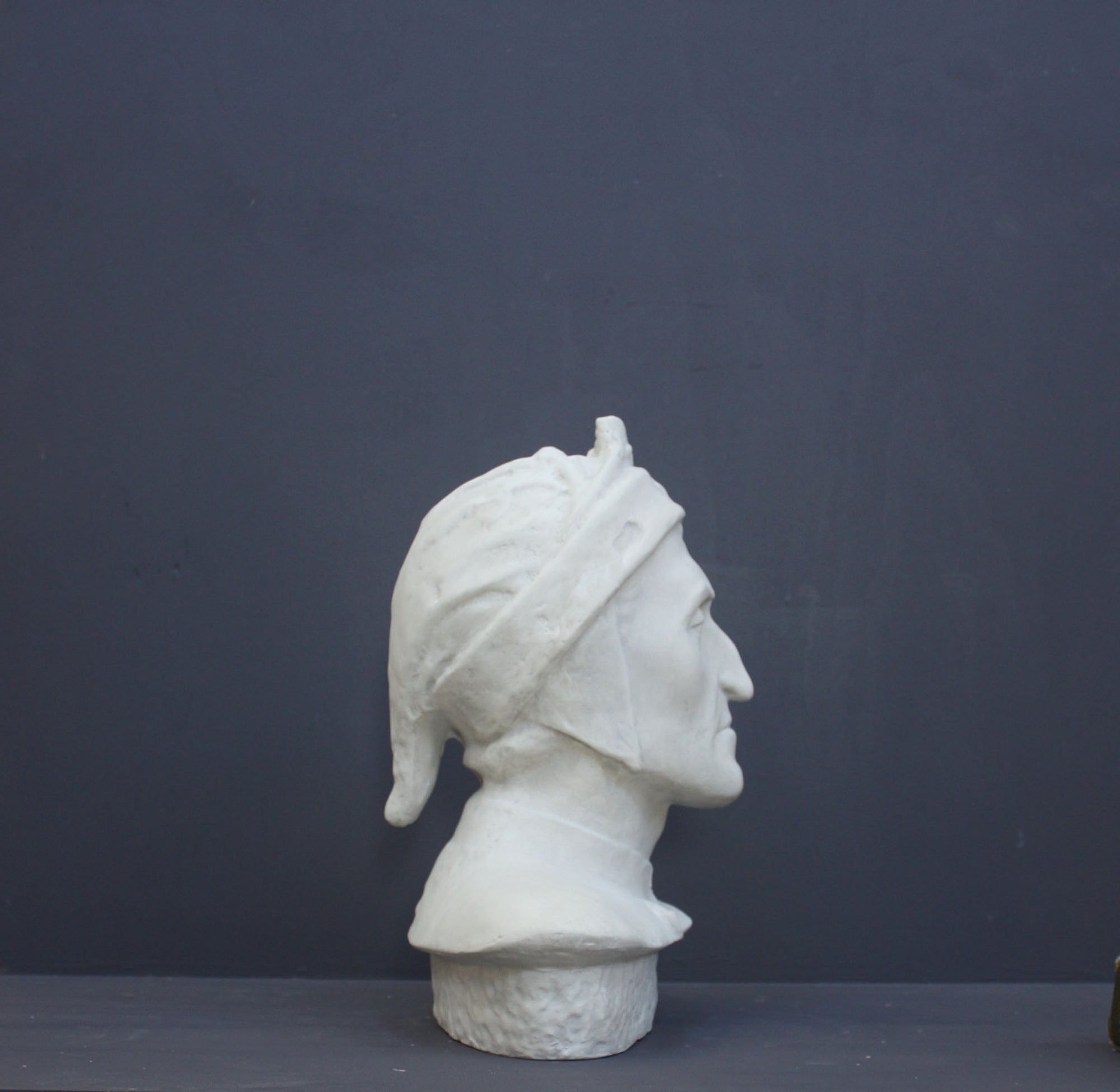 photo of plaster cast bust sculpture of Dante Alighieri with cap and high-necked robe with red book leaning against right side on black background