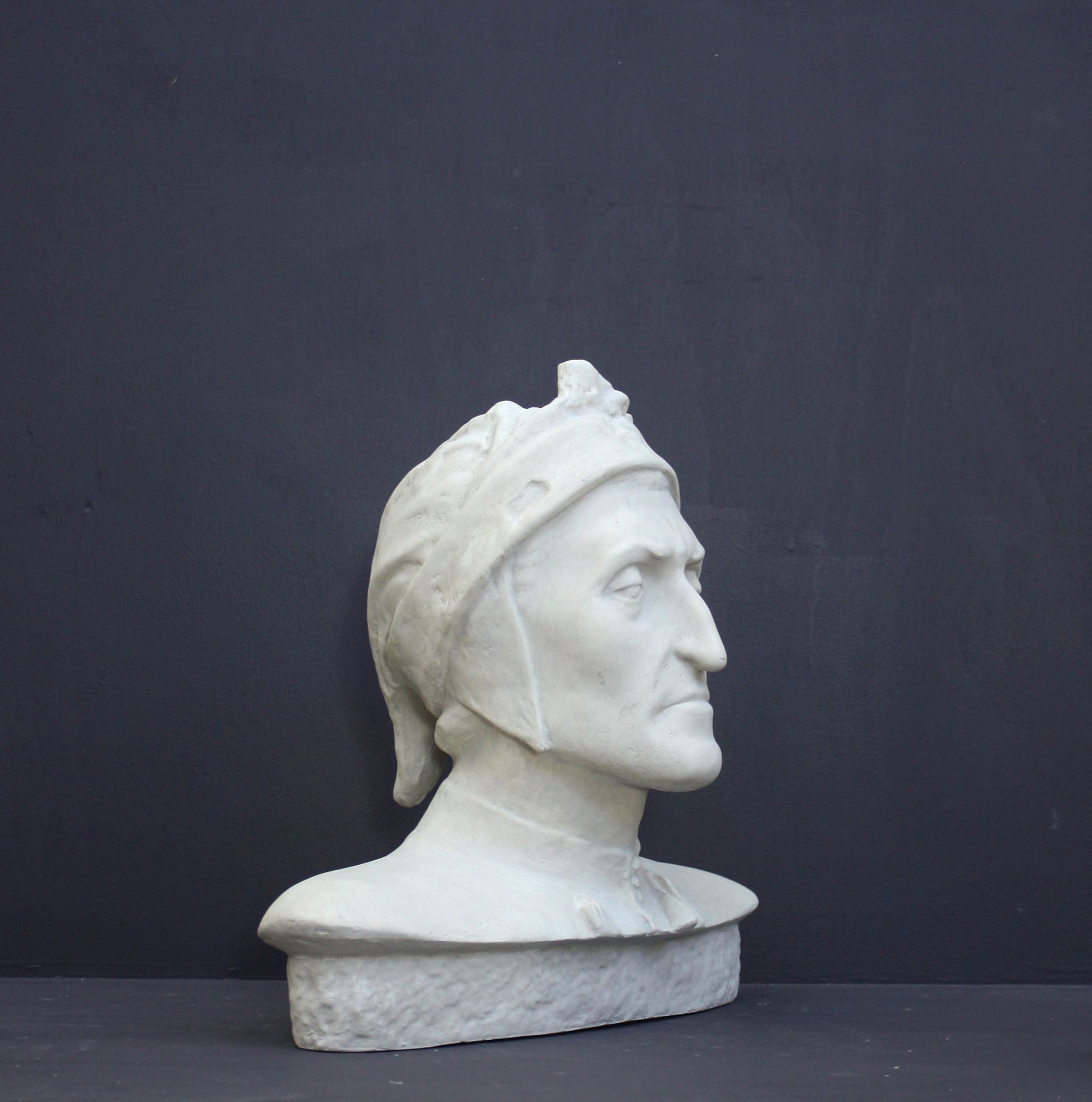 photo of plaster cast bust sculpture of Dante Alighieri with cap and high-necked robe with red book leaning against right side on black background