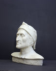 photo of plaster cast bust sculpture of Dante Alighieri with cap and high-necked robe with red book leaning against right side on black backgtround