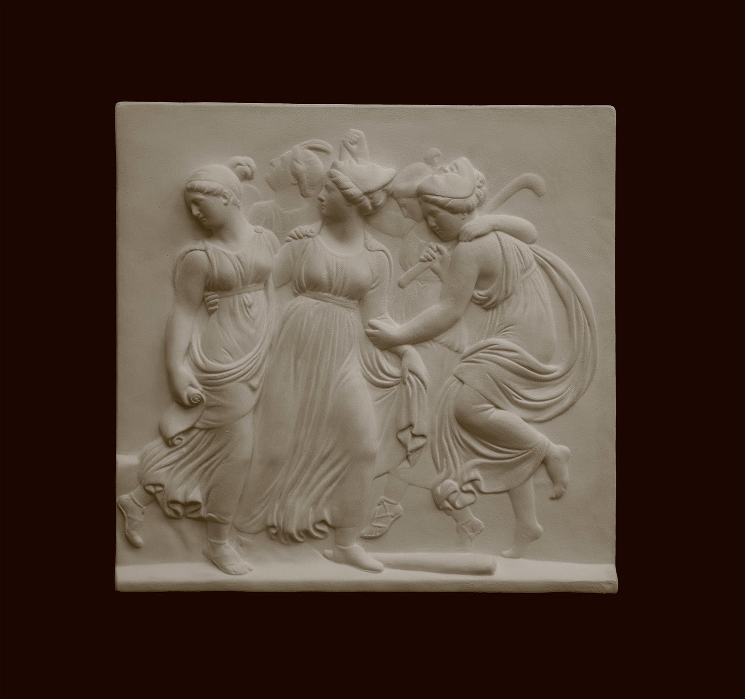 Photo with black background of plaster cast sculpture relief of females dancing