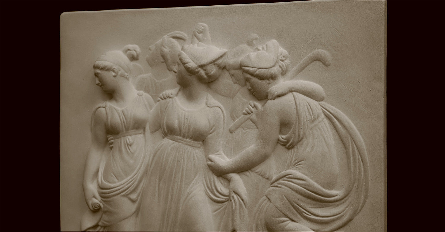 Photo with black background of plaster cast sculpture relief of females dancing
