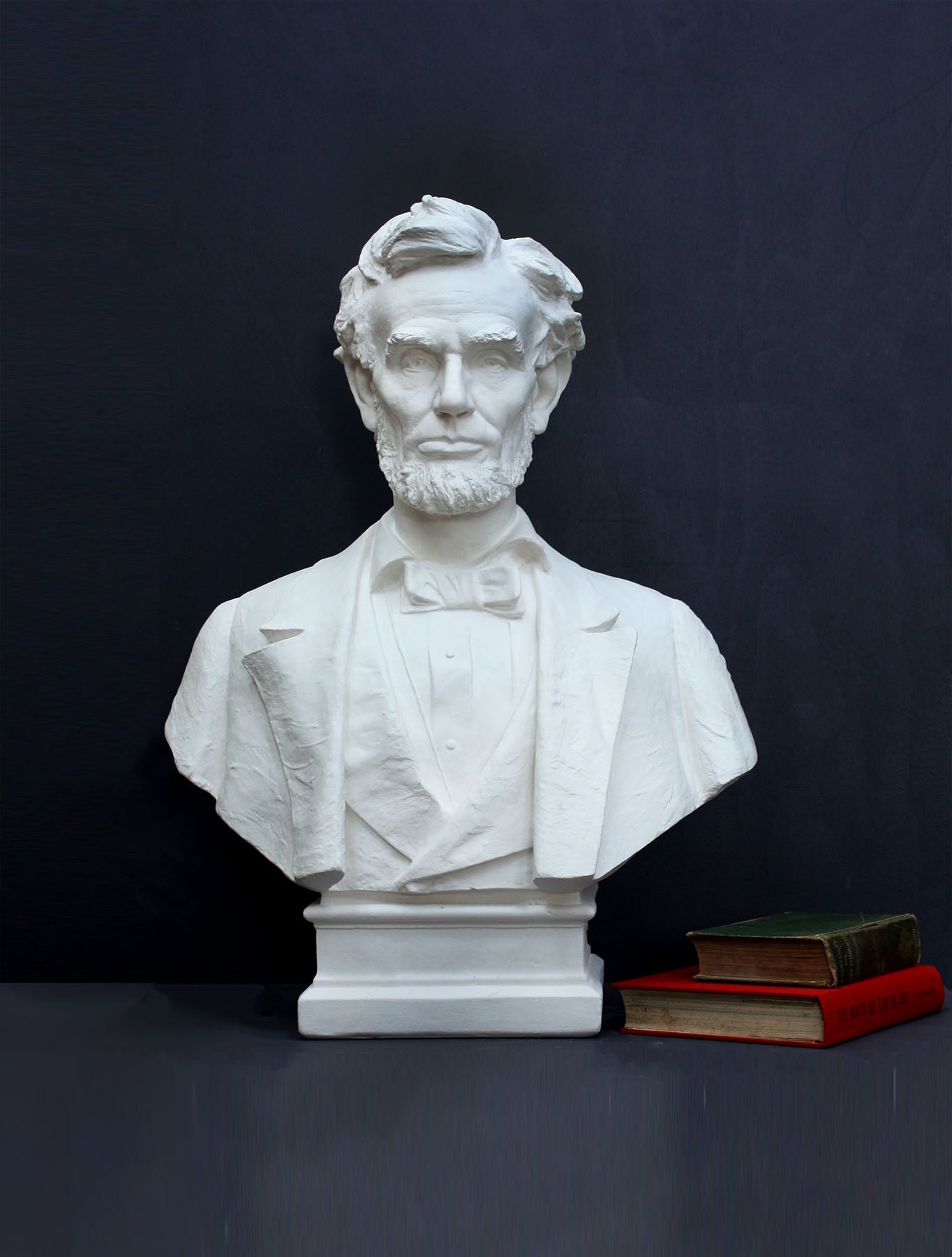 image of a plaster statue of a bust of lincoln next to books on a gray background