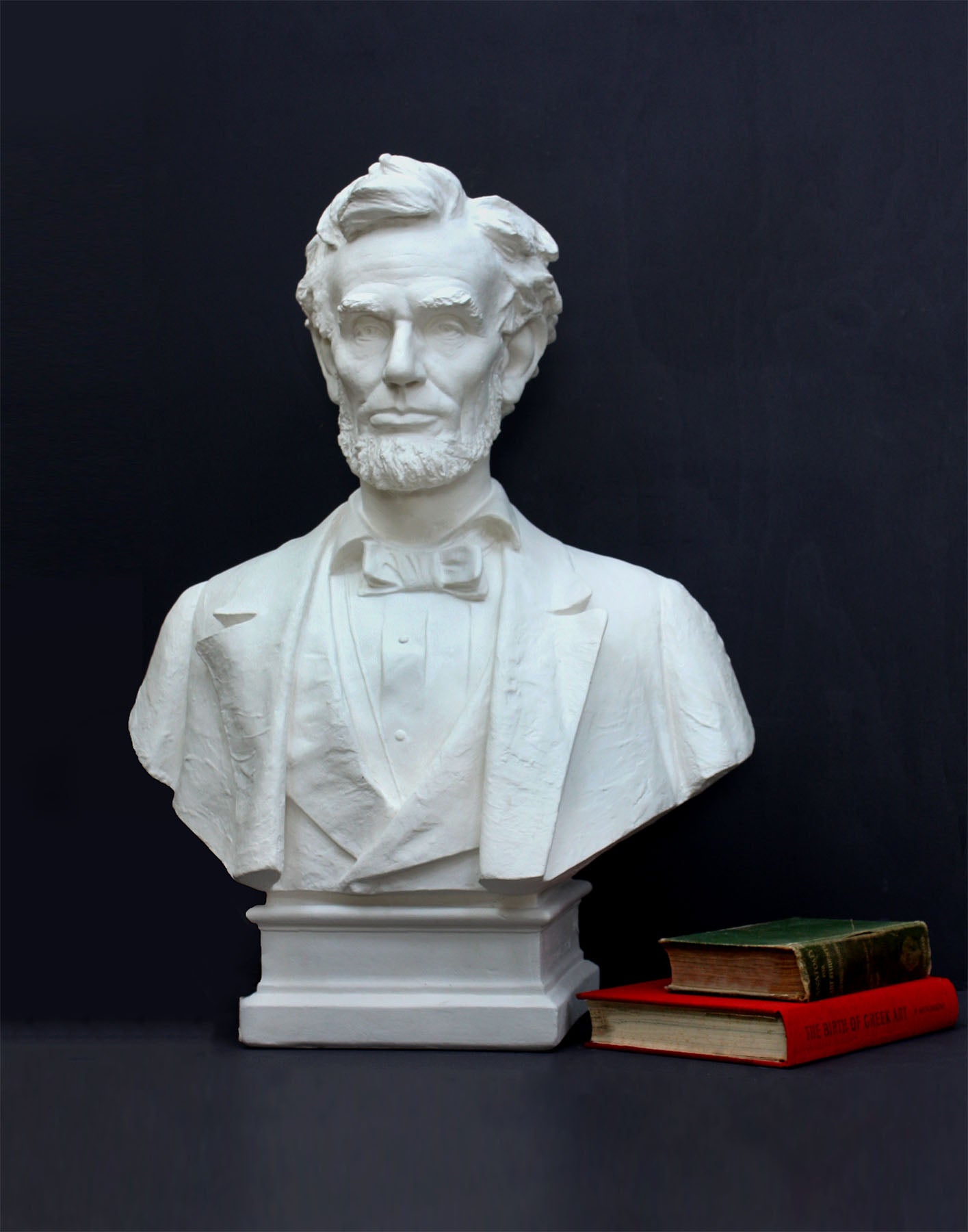 image of a plaster statue of a bust of lincoln next to books on a gray background