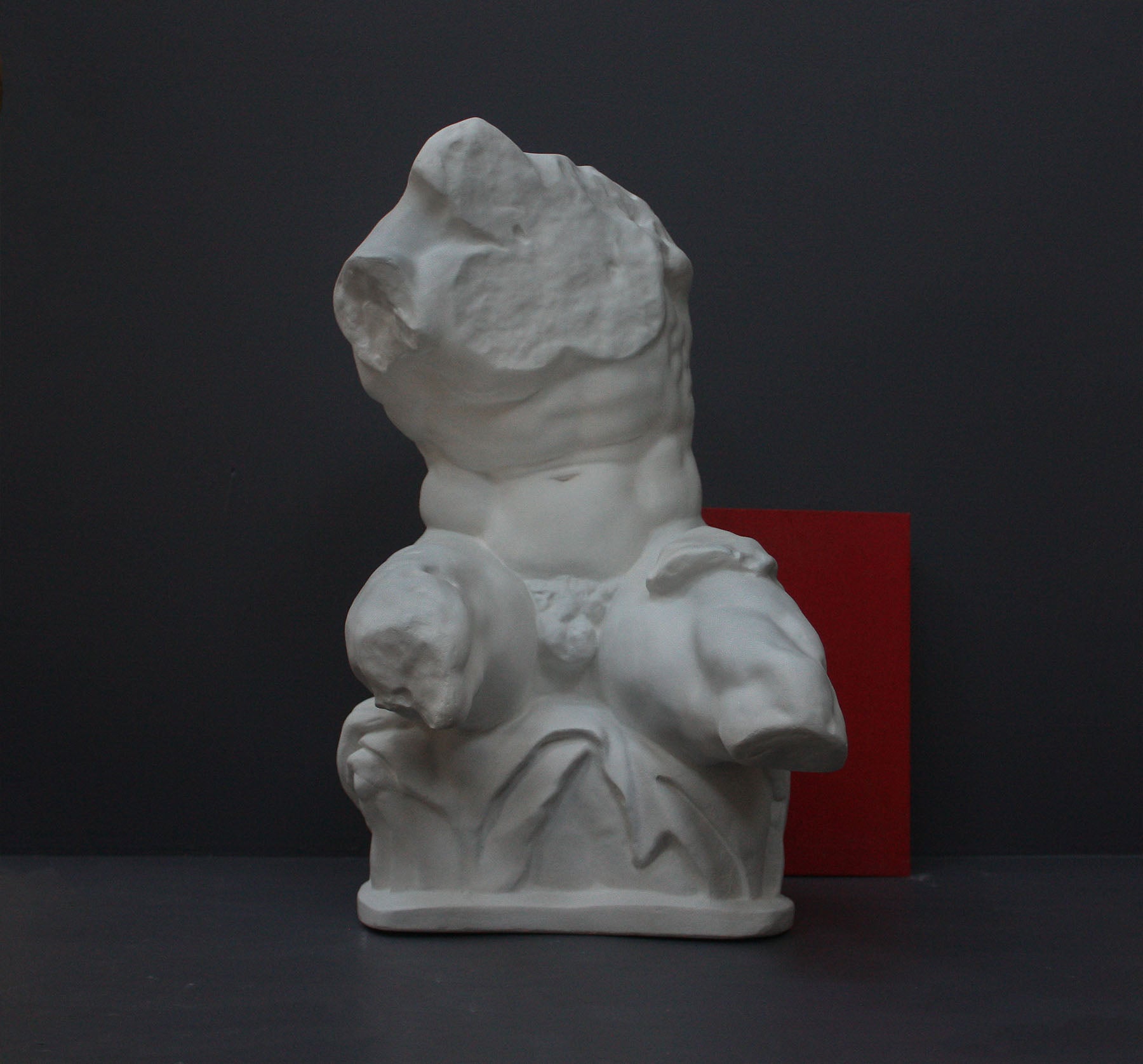 image of a plaster sculpture of nude male torso next to a red book on a gray background
