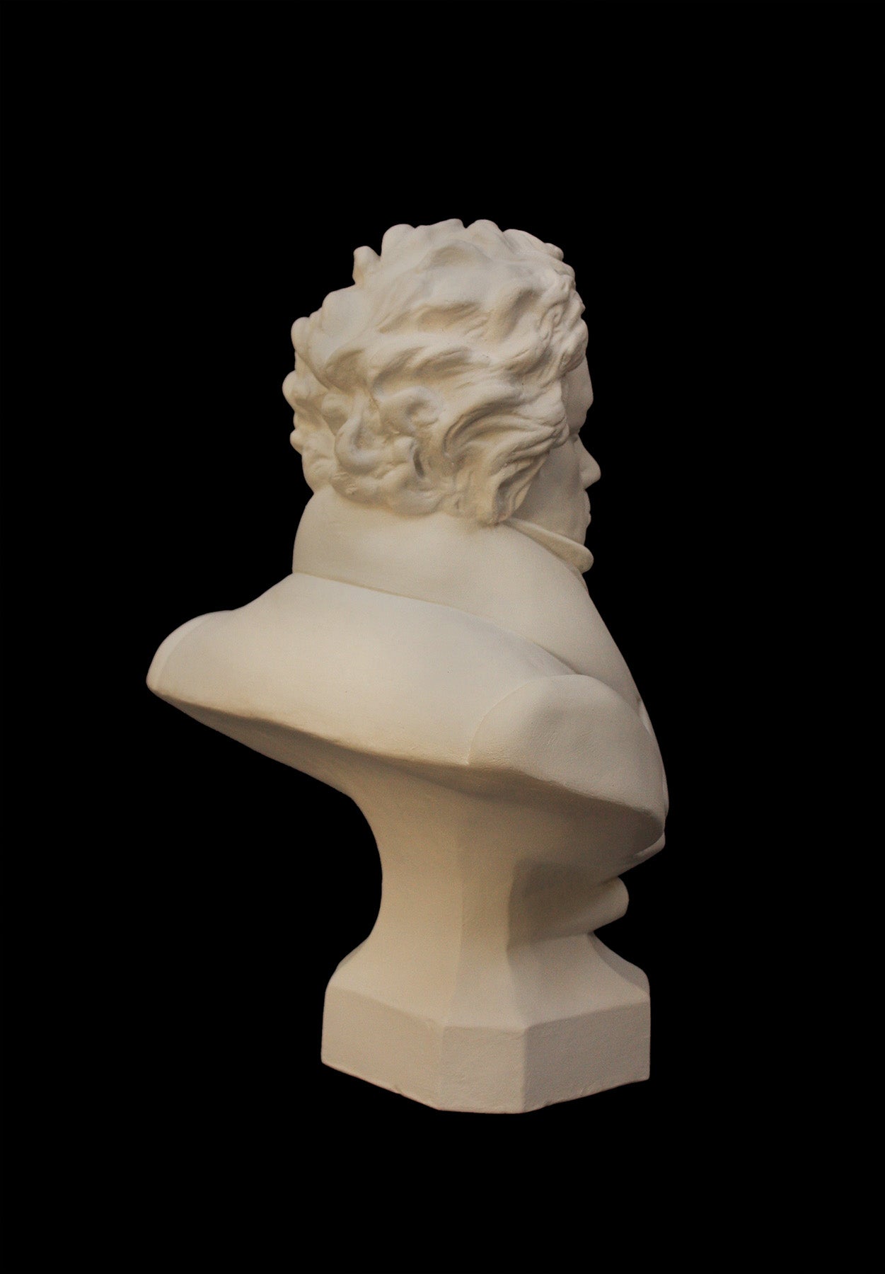back view photo of plaster cast sculpture of male bust of Ludwig van Beethoven in dress coat and ruffled necktie on black background