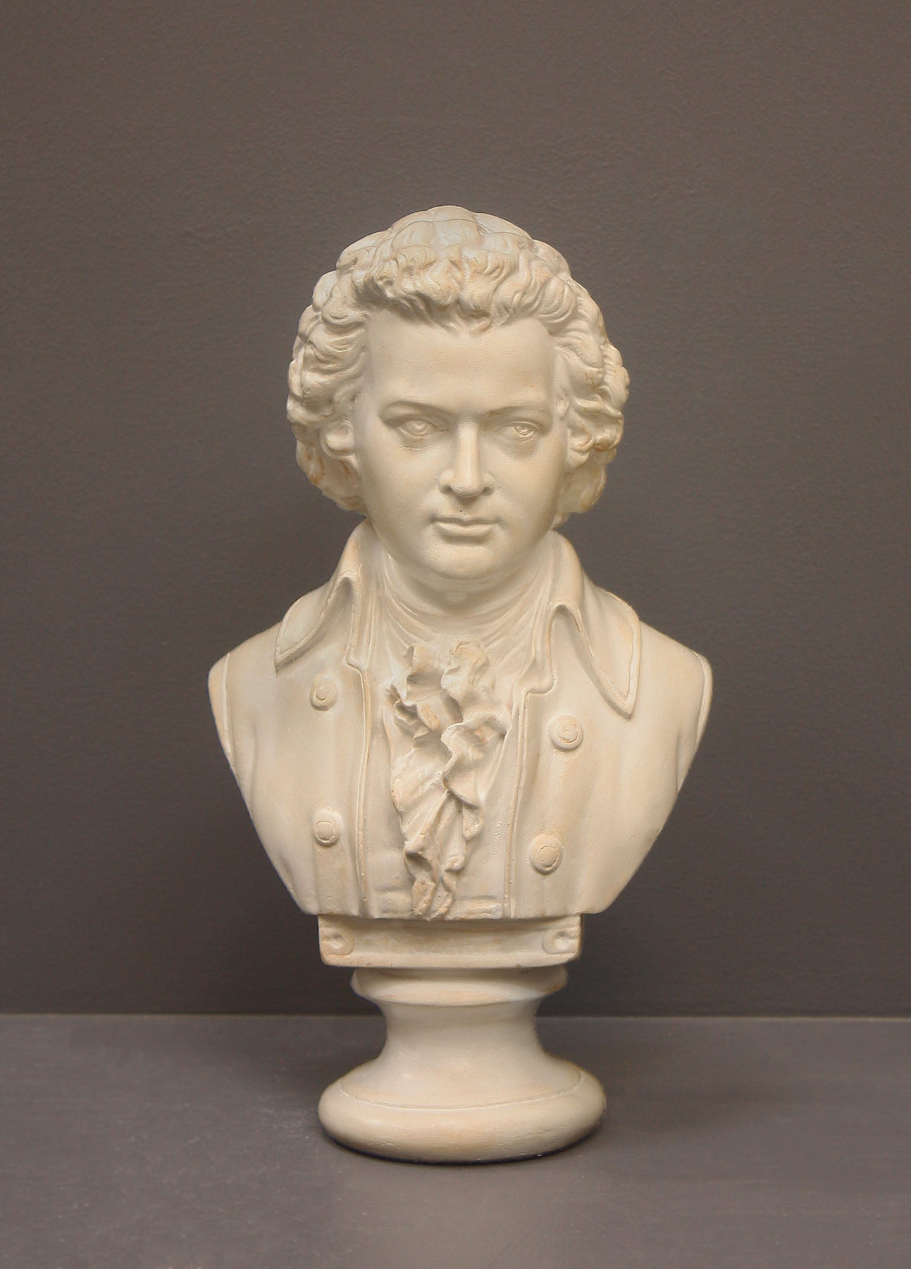 image of a plaster sculpture bust of man, namely Mozart, with ruffled necktie and coat on a gray background