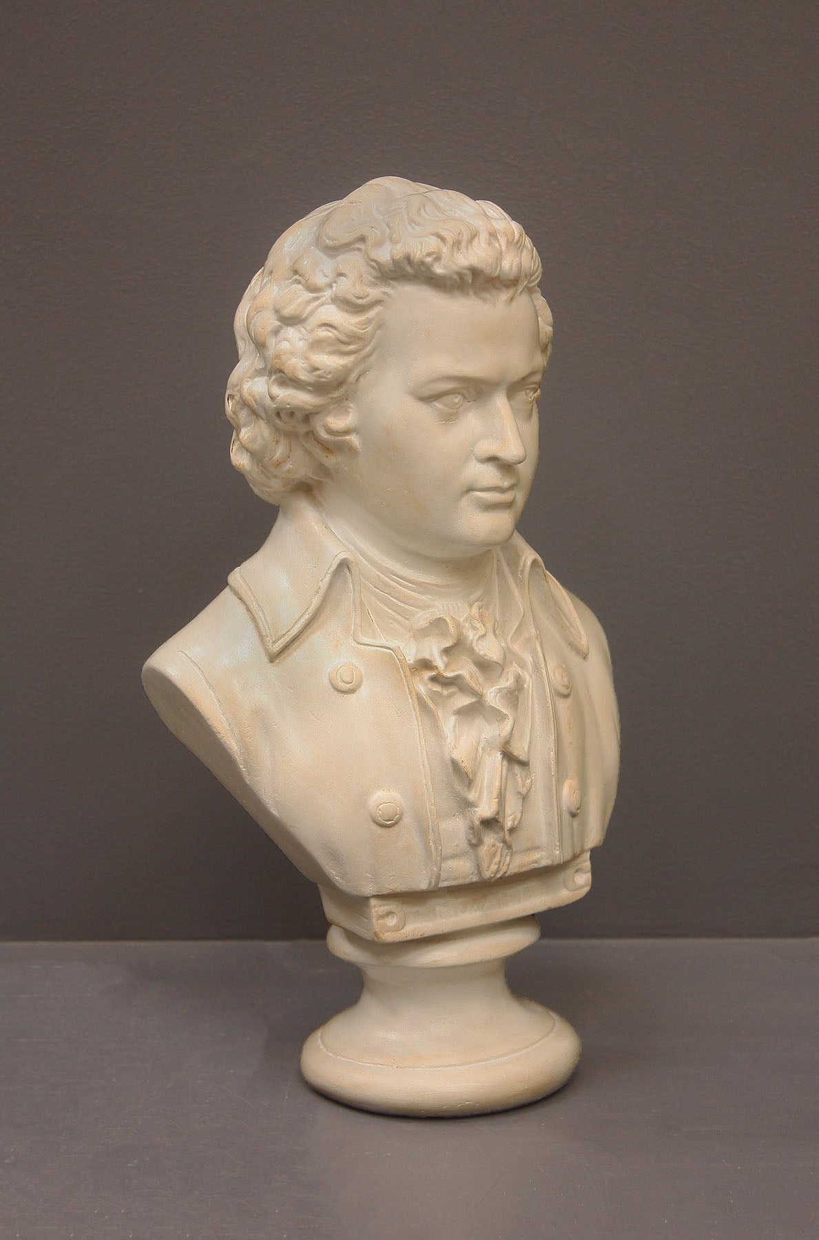 image of a plaster sculpture bust of man, namely Mozart, with ruffled necktie and coat on a gray background