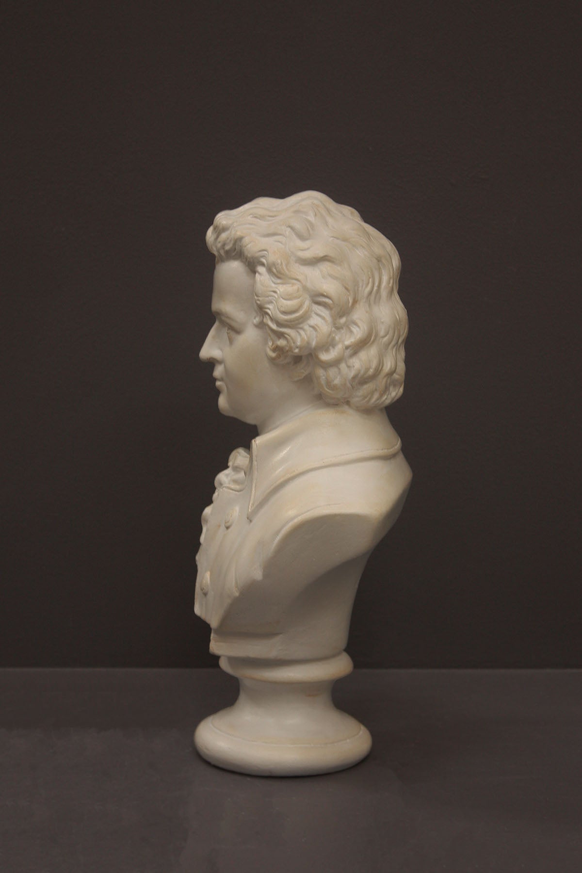 image of a plaster sculpture bust of man, namely Mozart, with ruffled necktie and coat on a gray background