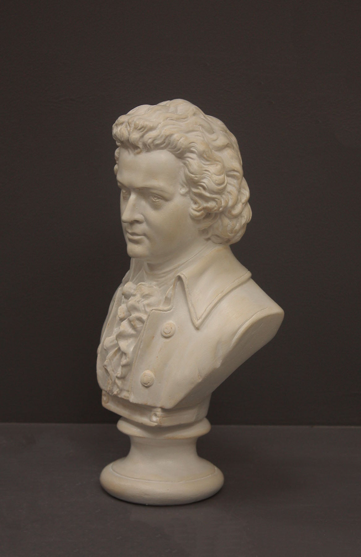 image of a plaster sculpture bust of man, namely Mozart, with ruffled necktie and coat on a gray background